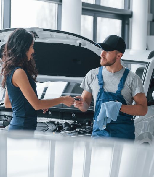 Trust and occupation. Woman in the auto salon with employee in blue uniform taking her repaired car back.